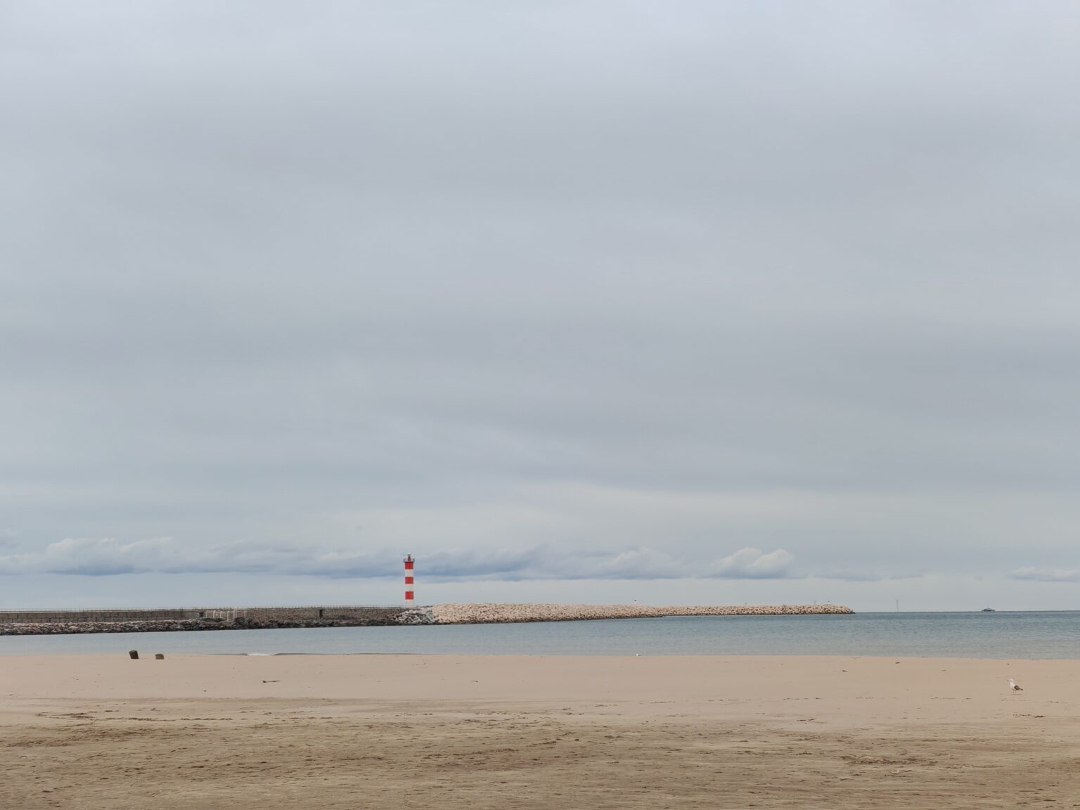 Empty sandy beach at Port-la-Nouvelle with the red and white lighthouse on the pier