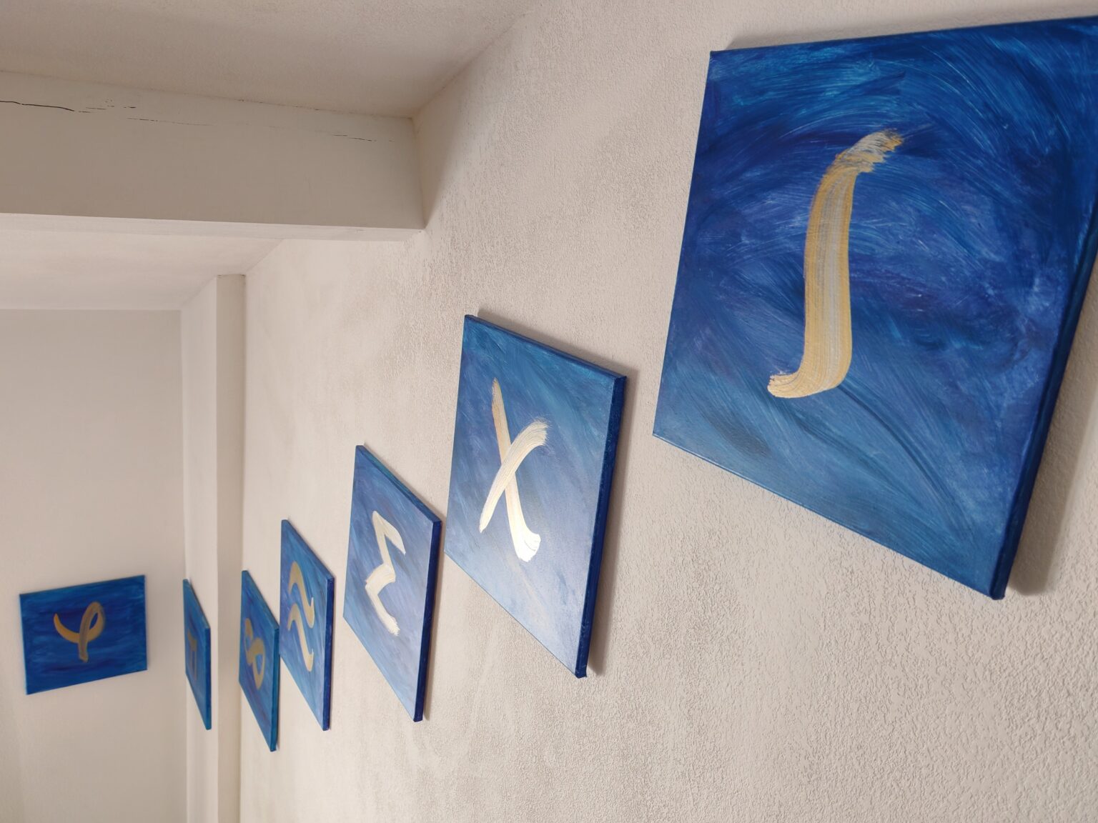 Blaue Leinwände mit goldenen Buchstaben an einer weißen Wand