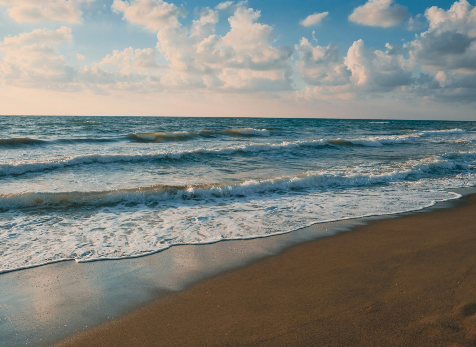 Wellen, die unter blauem Himmel an einen Sandstrand rollen