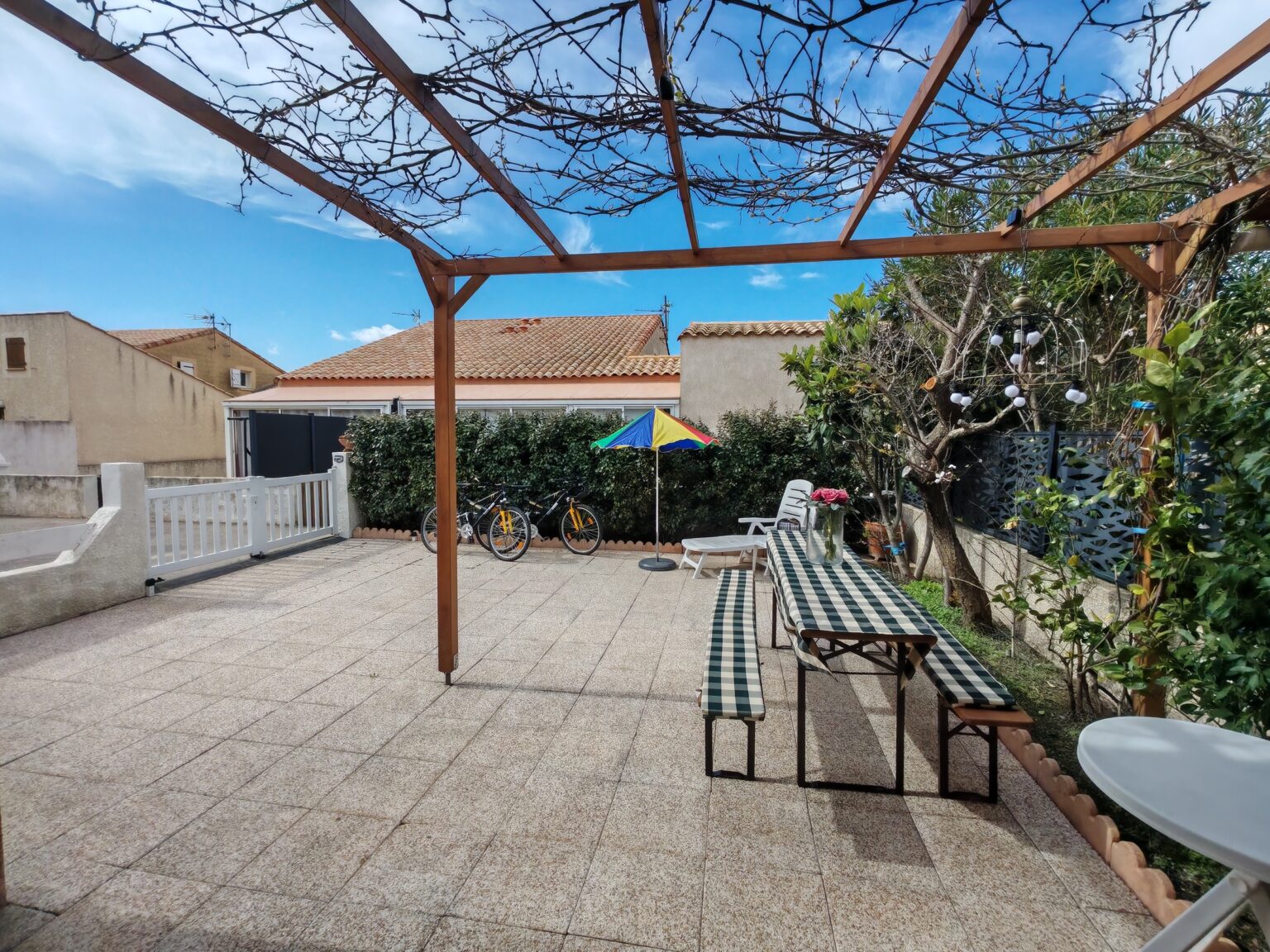 Sonnige Terrasse unter der Weinlaub-Pergola mit Holztisch und Bänken