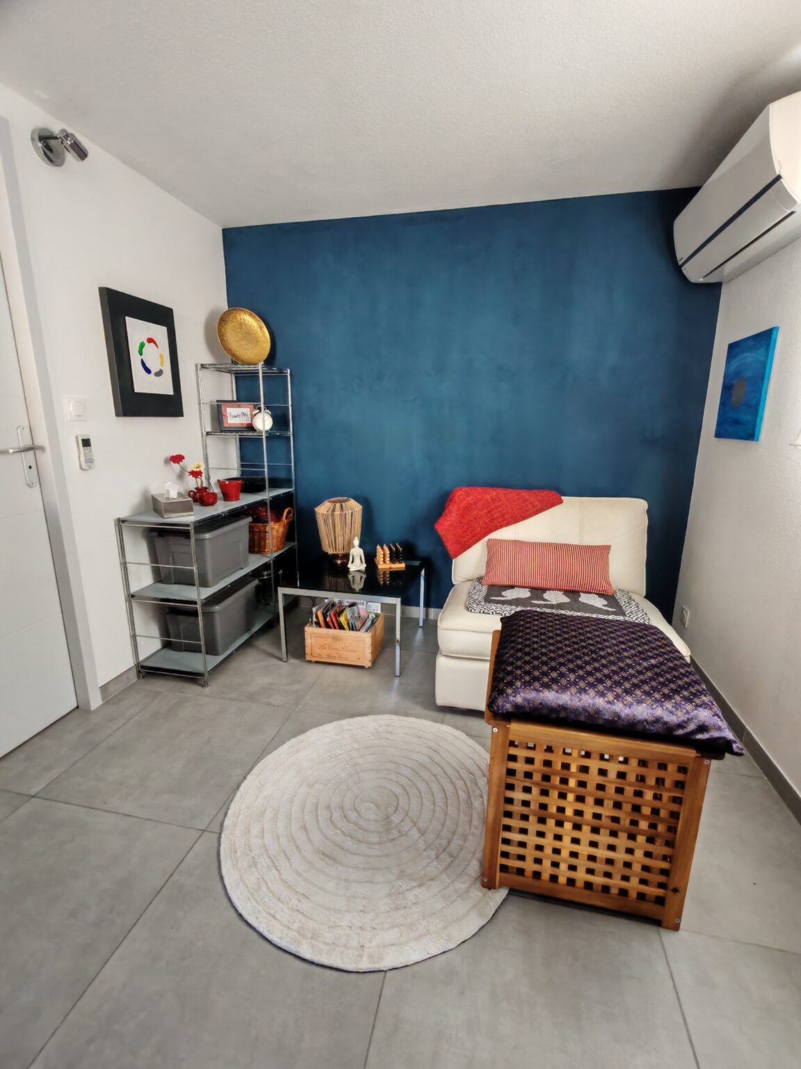 Zimmer mit blauer Akzentwand, Tagesbett, Rattanhocker und rundem Teppich