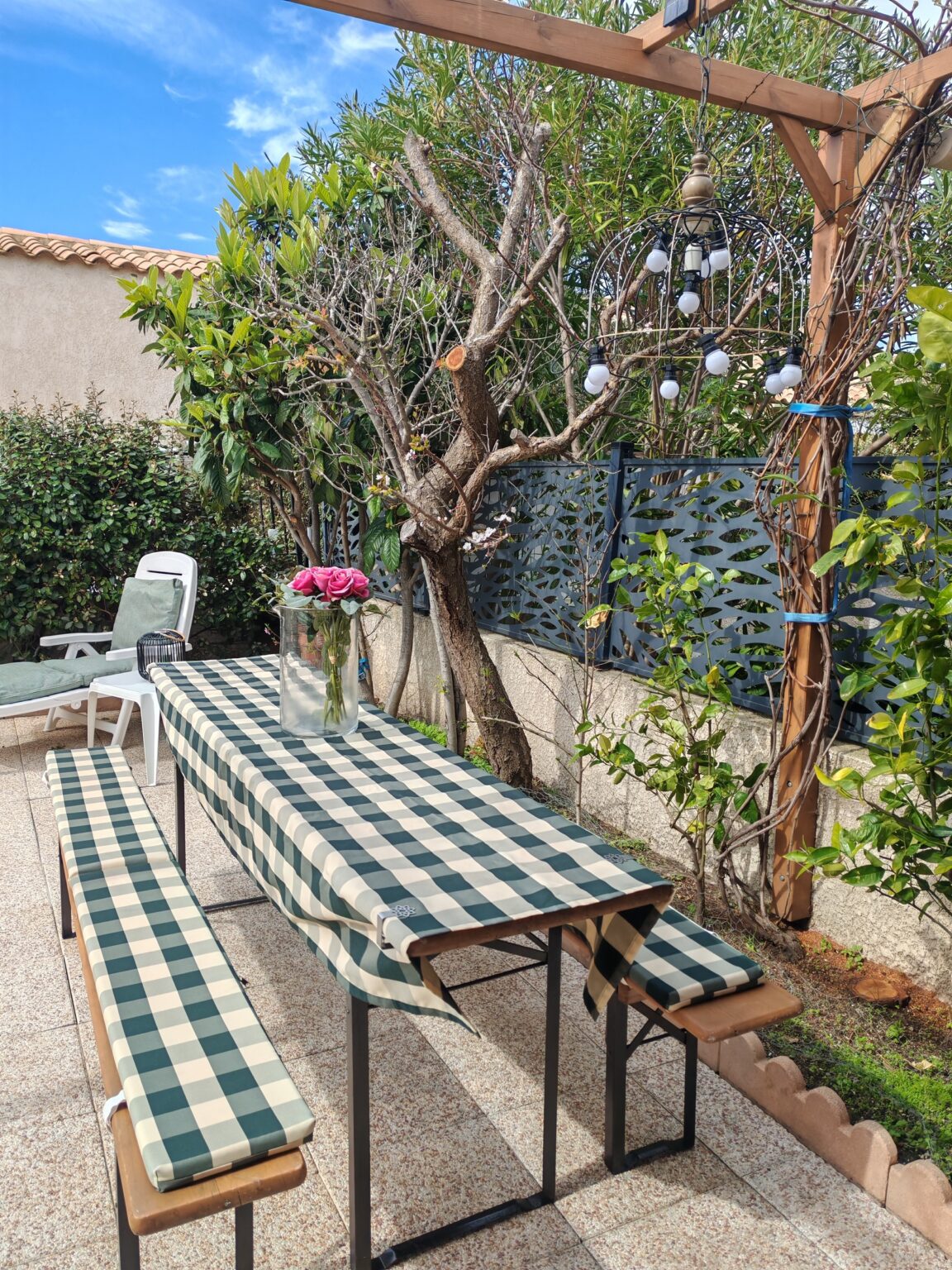 Gartenterrasse mit kariertem Tischtuch und Bänken unter Bäumen