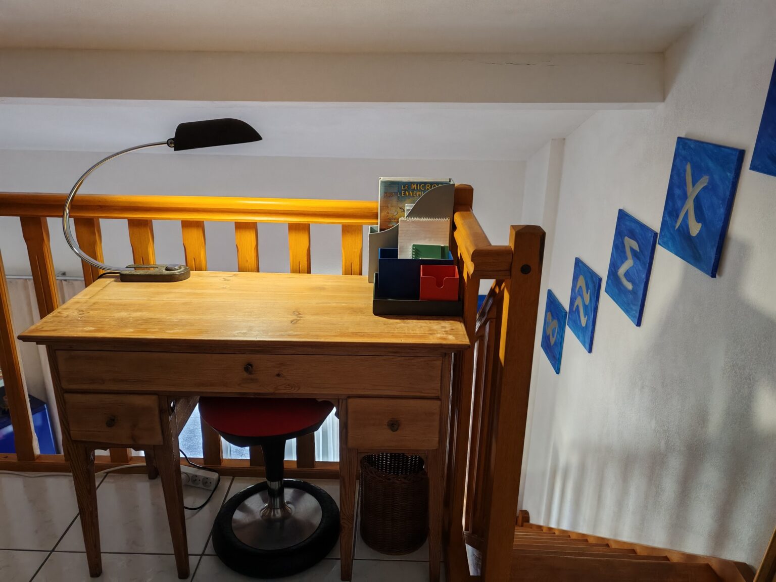 Holzschreibtisch mit Lampe und Stuhl unter blauen Kunstwerken