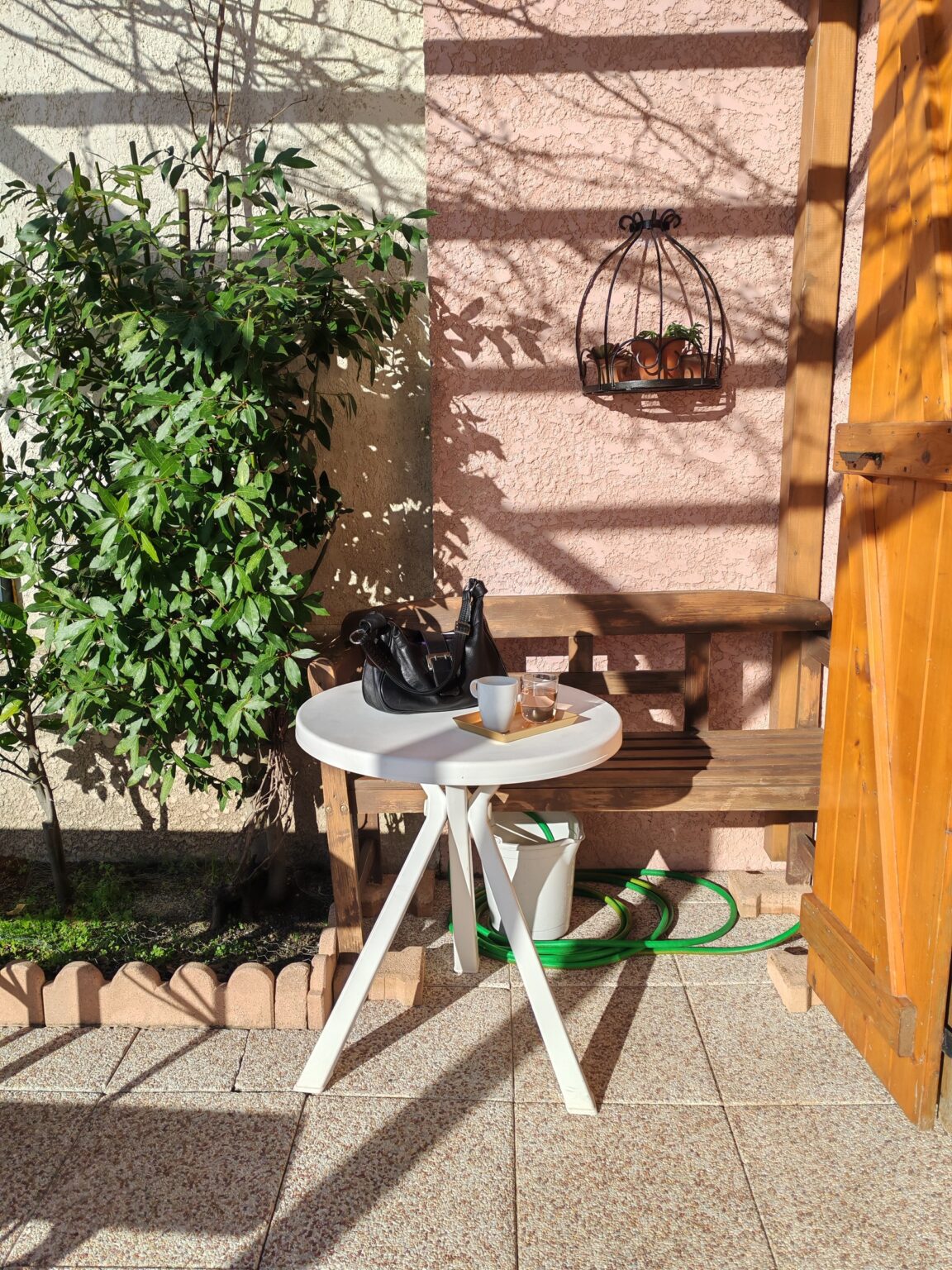 Rosa Innenhof mit Kletterpflanzen, kleinem weißen Tisch und Holztür